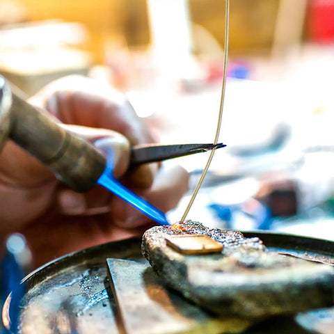 Focusing on the Top Tier Copper Welding Rods Kit 4pcs for Jewelry Making, a welder using a torch to solder metal.