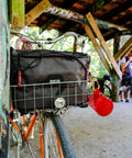 4 In 1 Dayliner Box Bag 20 Liter Water Resistant Rolltop attached to a bike basket under a wooden shelter, ideal for commutes and camping