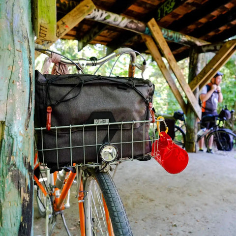 4 In 1 Dayliner Box Bag 20 Liter Water Resistant Rolltop attached to a bike basket under a wooden shelter, ideal for commutes and camping