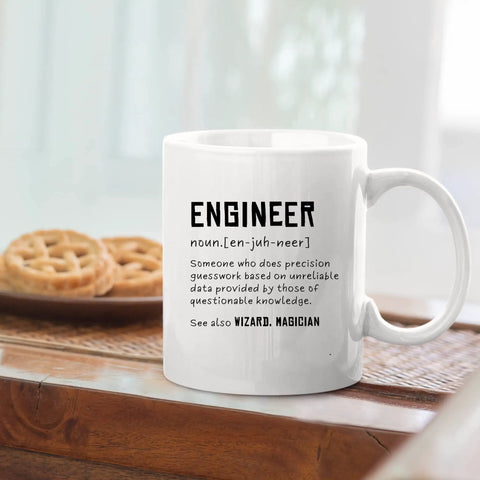 Engineer Definition Funny Gift Mug For Engineering Students Teachers And Pros Nerdy Computer Civil Mechanical Electrical Software Engineers 11 Oz White Ceramic Coffee Mug on table with pie