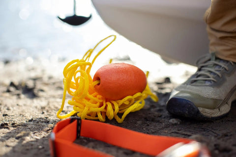 Orange Nautical Safety Kit For Paddle Sports And Boating No Brainer Gear With Waterproof Headlamp on ground by water