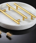 Three gold cabinet handles displayed on a white marble tray