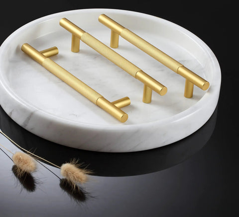 Three gold cabinet handles displayed on a white marble tray