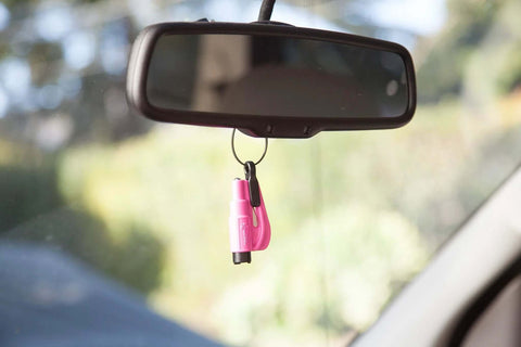 Resqme emergency escape tool, pink, on a key ring hanging from car rearview mirror.