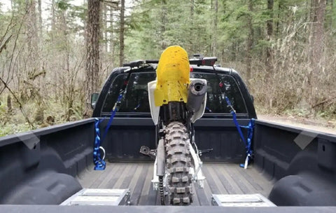 Heavy Duty 6 Pack Ratchet Straps Tie Down Haulers 1 Inch X 12 Foot With S Hooks securing a dirt bike in a truck bed surrounded by trees.