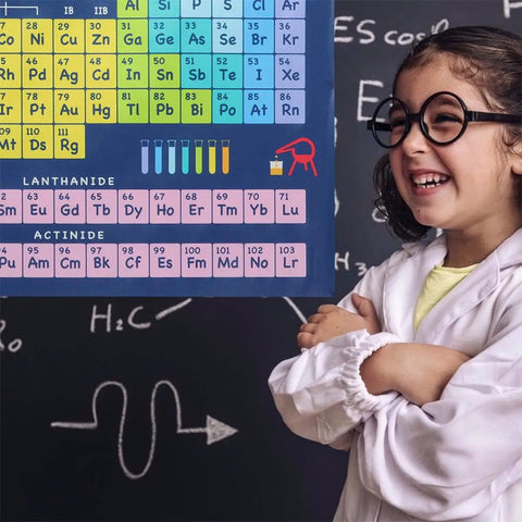 Smiling child in lab coat next to Periodic Table Of Elements Poster Set 2 Pieces 40x60cm Classroom Educational Chart with symbols and uses.