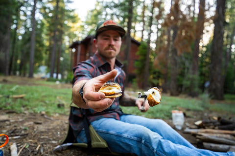 Man offering s'more while sitting on lightweight outdoor chair for stadium seats camping hiking and more water resistant adjustable straps