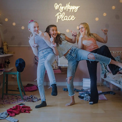 Three girls in a bedroom with My Happy Place Neon Sign Warm White Neon Lights For Bedroom Decor Cozy Home Office Wall Art Wedding And Birthday Party Decor Gift For Girls Room Modern Neon Wall Sign glowing above.
