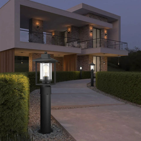 Boss Black Outdoor Post Light With Clear Glass Shade illuminating a modern walkway outside a contemporary home in the evening.