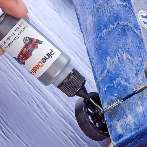 Applying graphite lubricant from Derby Pinewood Car Weights Kit With 14 Cylindrical Tungsten Weights Across 4 Sizes onto blue car wheel.