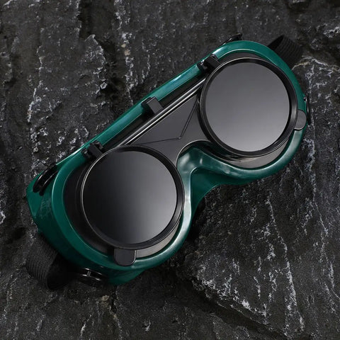 Four Pack Heavy Duty Welding Safety Goggles With Anti Scratch Coating And Double Flip Up Lenses viewed from above on rough surface.