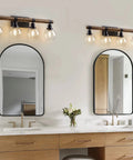 Farmhouse Wood Vanity Light Fixture With Four Lamps Over Mirror, Rustic Sconce Lighting With Clear Glass Shades in bathroom setting