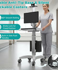 Game Changer Height Adjustable Medical Computer Cart With Sturdy Monitor Mount And Smooth Ride Wheels; woman using the mobile workstation in a hospital corridor.