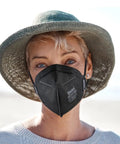 Woman wearing NIOSH Approved N95 Face Mask for Adults, 30 Pack, Five Layer Filtration, on a beach, breathing easily, reusable style.