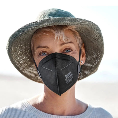 Woman wearing NIOSH Approved N95 Face Mask for Adults, 30 Pack, Five Layer Filtration, on a beach, breathing easily, reusable style.