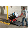Worker using drum modular spill platform for customizable spill control, heavy duty build, 26.25 x 26 x 6.5 inches, 15 gallon sump, 2000 lb load capacity containment tray, made in USA, yellow, 1633 in a warehouse setting.