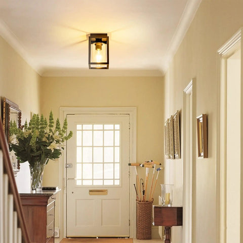 Flush Mount Ceiling Light Fixture With Clear Glass Shade In A Farmhouse Black Metal Frame, installed in a bright entryway.