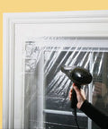 Person using a hairdryer on an Indoor Shrink Window Kit 42 Inch By 62 Inch Three Sheet Set Easy Install Window Insulation Solution For Drafty Homes Weatherproof And Energy Saving Now.