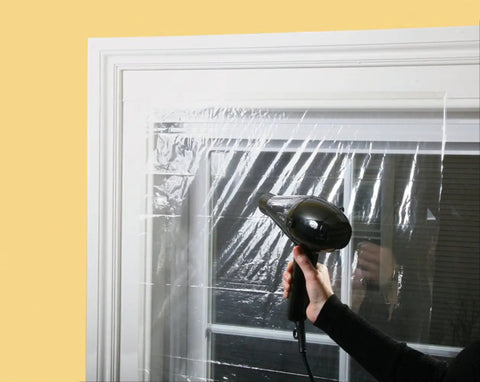 Person using a hairdryer on an Indoor Shrink Window Kit 42 Inch By 62 Inch Three Sheet Set Easy Install Window Insulation Solution For Drafty Homes Weatherproof And Energy Saving Now.