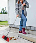 Person using Heavy Duty Long Handle Outdoor Broom 62 Inch For Tough Yard Work And Garage Cleanup to sweep leaves off driveway.