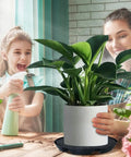 Child and woman caring for plant on Self Watering Pot Base With Automatic Irrigation System For Indoor Outdoor Gardens And Greenhouses Hassle Free Setup Durable PP Plant Tray Waterproof Stand For Pots On Patio Yard Balcony And Farm Pathways