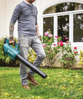 Person using Powerful 18V Cordless Blower Kit With 459 CFM 116 MPH Brushless Motor outdoors on grass next to flower bushes