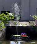 Solar Fountain Pump 1.5W Upgraded Submersible Water Panel Kit With 4 Nozzles For Bird Bath Small Pond Garden And Lawn No Battery Or Electricity Needed Auto Runs In Sunlight, installed in a garden pond with plants around.