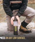 Demonstration of GeoPress 24 Oz Water Purifier Bottle For Hiking And Camping in use on a sandy surface near a river.