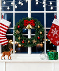Christmas wreath with red and gold ornaments, striped and snowflake stockings, and festive decorations on window sill