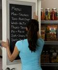 Person placing a chalkboard menu on a pantry door with jars and baskets on shelves inside.