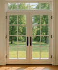 Glass double doors with black barn door handles installed in a bright room overlooking green trees and lawn.