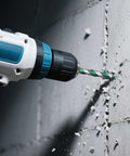 Masonry drill bit in blue cordless drill boring into concrete wall; green and silver tungsten carbide bit.