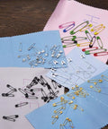 Kickass Assorted Steel Safety Pins Bulk Kit For Sewing Tailoring And Crafting on colored fabric swatches.