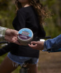 Hands exchanging On The Go S'mores Portable Campfire Kit For Easy Outdoor Treats, perfect for camping, in a wooded area