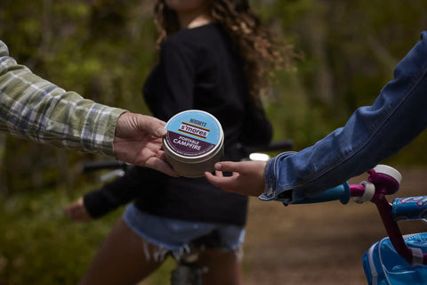Hands exchanging On The Go S'mores Portable Campfire Kit For Easy Outdoor Treats, perfect for camping, in a wooded area