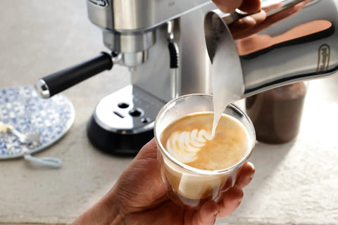 Stainless Steel Milk Frothing Pitcher 17 Oz With Ergonomic Double Grip Handle Easy Pour Spout For Latte Art Dishwasher Safe Ideal For Home Barista Coffee And Cappuccinos pouring milk into a coffee cup creating latte art.