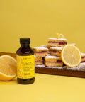 Lemon bakery emulsion bottle with sliced lemon and powdered dessert, part of Bakery Emulsion Variety Pack For Cakes, Cookies And Desserts With Flavors Almond, Butter Vanilla, Lemon, Princess Cake And Cookie, Red Velvet, Strawberry Gluten Free And Keto Friendly, 4 Oz Bottles A Must Have For Home Bakers.