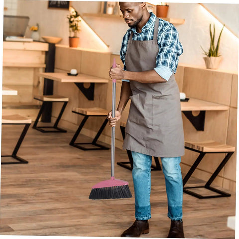 Legit Heavy Duty Pink Broom With Sturdy Steel Handle And Ultra Soft Bristles For Zero Sweat Indoor And Outdoor Floor Cleanup Compact Reusable Dust Brush That Really Cleans in use by a man in an apron.