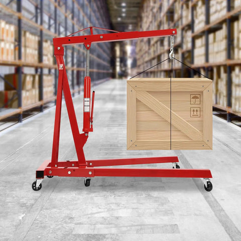 Heavy Duty Folding Hydraulic Engine Hoist Built Tough As Nails With Six Swivel Casters Telescopic Boom lifting a wooden crate in a warehouse.