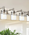 Four Light Vanity Light In Brushed Nickel With Clear Glass Shades mounted over a bathroom mirror reflecting light.