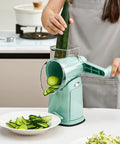 Person using Rotary Cheese Grater Hand Crank 5 In 1 Mandoline Slicer With 5 Stainless Steel Blades to slice cucumber in kitchen.