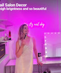 Woman using makeup in beauty studio with Pink Neon Nail Sign For Nail Salon And Beauty Studio Decor LED Light Open Sign Wall Art Perfect For Nail Rooms, Beauty Bars, Spas, Shops, And Home Makeovers, Party Ready For Parties, Weddings, And Social Media Photo Ops glowing in the background.
