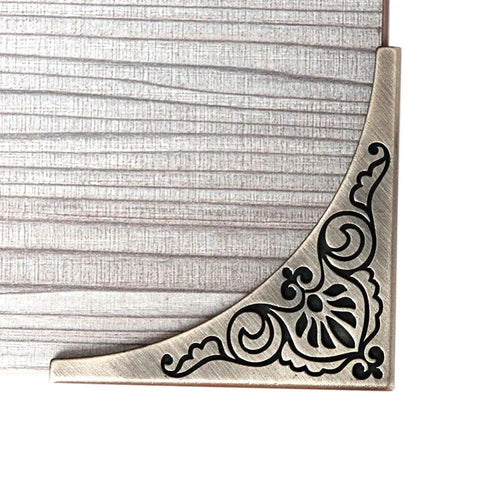 Antique Bronze Metal 4 Pack Corner Protectors Furniture Edge Guards With Classic Carved Details close-up view on wooden table corner.