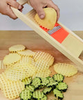Wave waffle crinkle cutter with wooden frame and orange blade slicing a potato; crinkle-cut potato slices and zucchini on board.