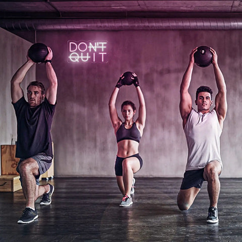 People exercising with weights under 'Don't Quit' neon sign in gym, potential man cave or office decor.