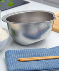 Stainless Steel Rice Washer Strainer Bowl With Agitator Bumps for quick no fuss rinsing, on a kitchen countertop near rice and chopsticks.