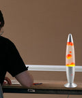 13 Inch Liquid Motion Lamp With Yellow Wax Flow In Clear Water on a desk beside a seated person, creating cozy vibes
