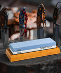 Premium Knife Sharpening Stone Whetstone 1000 6000 Grit With Non Slip Base on display with knives in background