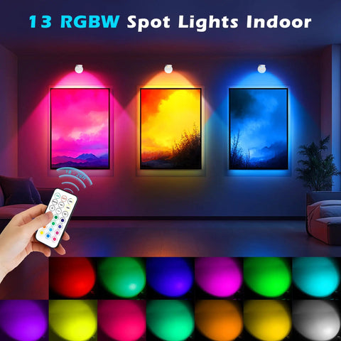 Colorful RGBW indoor spotlights illuminating framed artwork with a remote control. 2 Pack Rechargeable LED Spotlight Kit For Indoor Use With Wireless RGB Color Lighting, Remote Control, Magnetic Battery Powered Puck Lights, Ceiling Uplight With Rotatable Head For Plants, Portraits, And Artwork.