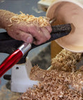 Carbide wood turning tool with a red aluminum handle on a wood lathe amid wood shavings